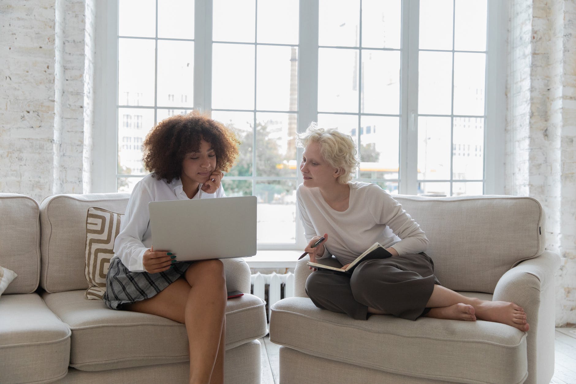positive young diverse girlfriends working on project together using laptop in apartment